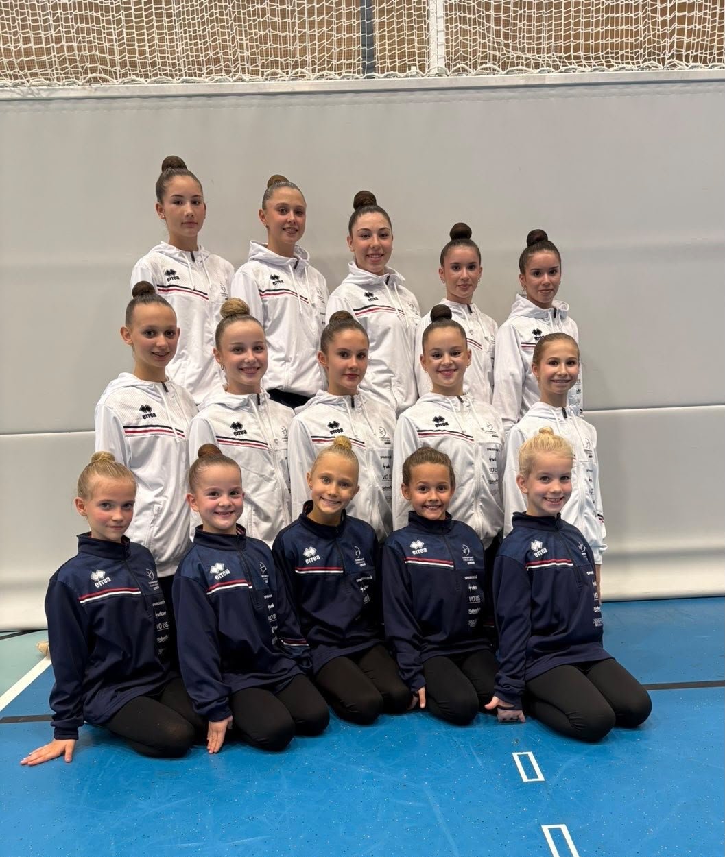 Gymnastikgruppe in Trainingskleidung posiert für ein Gruppenfoto in einer Halle.